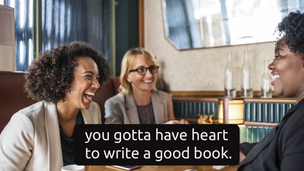 Two women of color at a restaurant table, nearly doubled over in laughter, with words saying, “It takes heart to write a good book.”